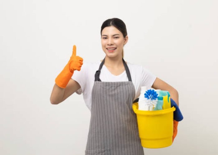 Young housekeeper woman holding bucket of cleaning products ready for cleaning home on isolated white background.